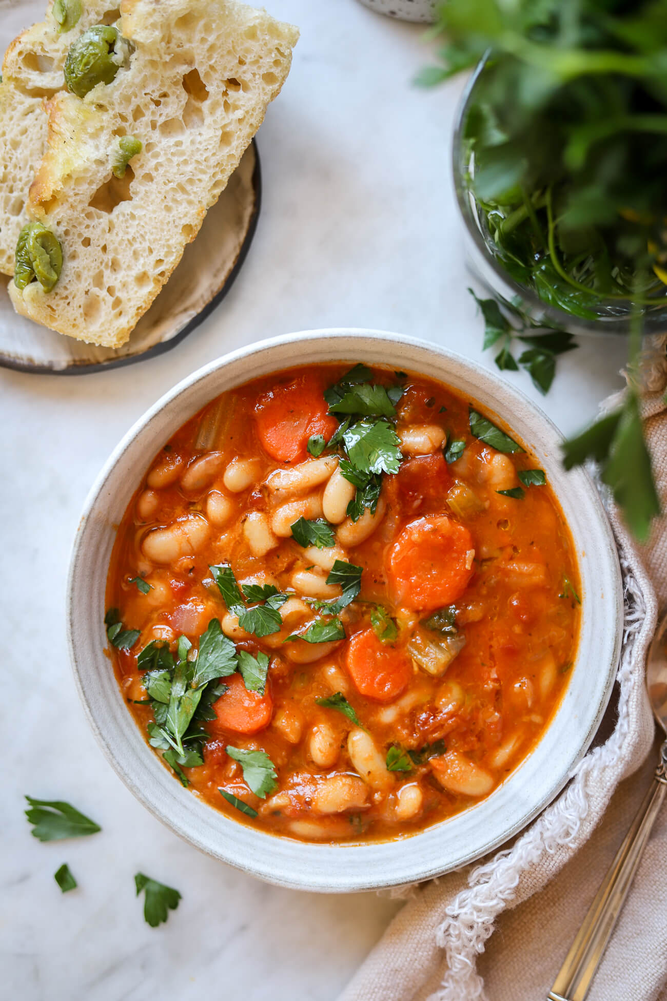 An overhead photo of Greek white bean soup in a bowl with olive focaccia on the side. A simple Blue Zone dinner recipe. 