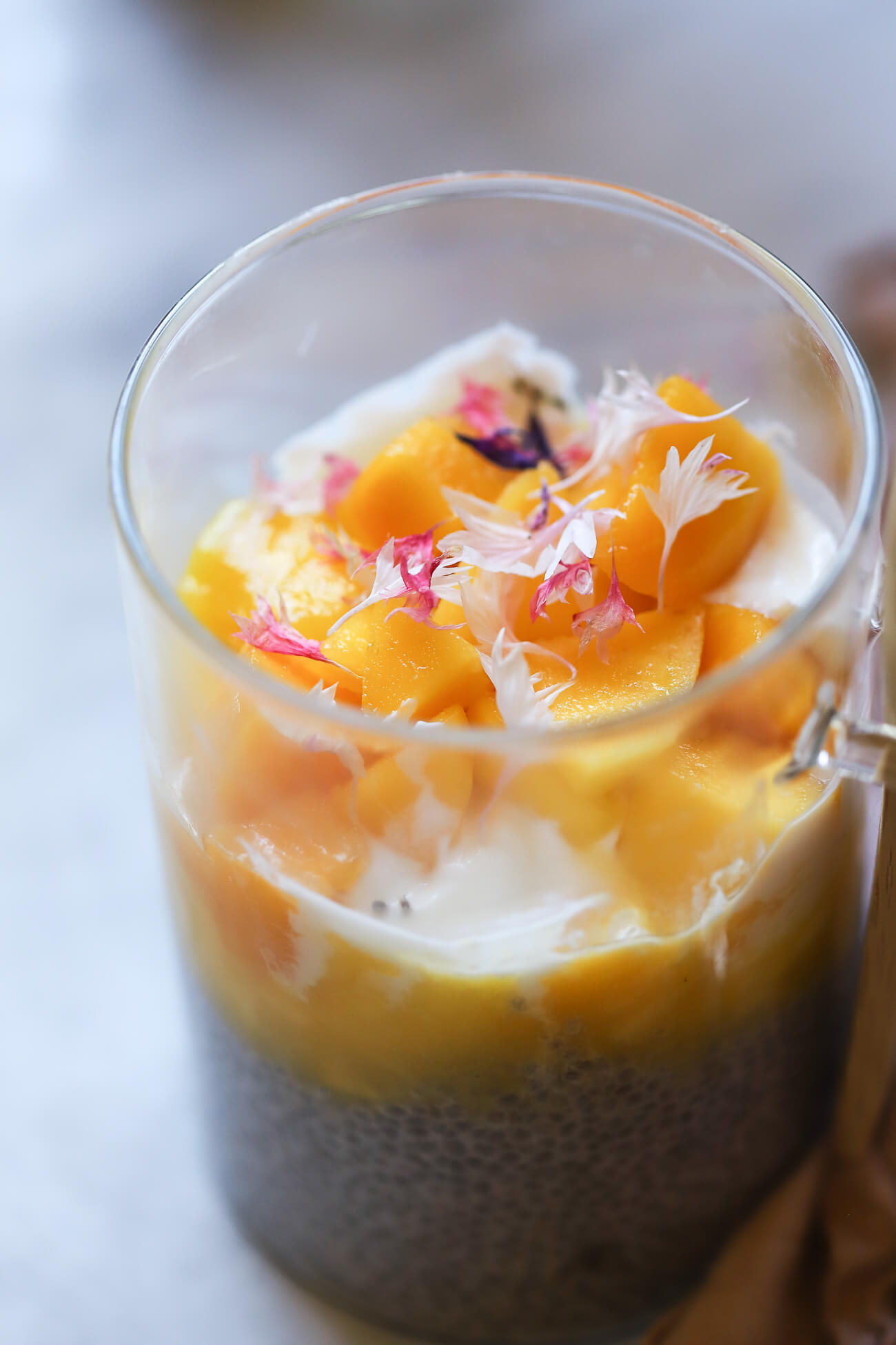 A close-up photo of fresh mango chunks atop chia pudding, mango puree, and plain yogurt in a clear serving jar. 