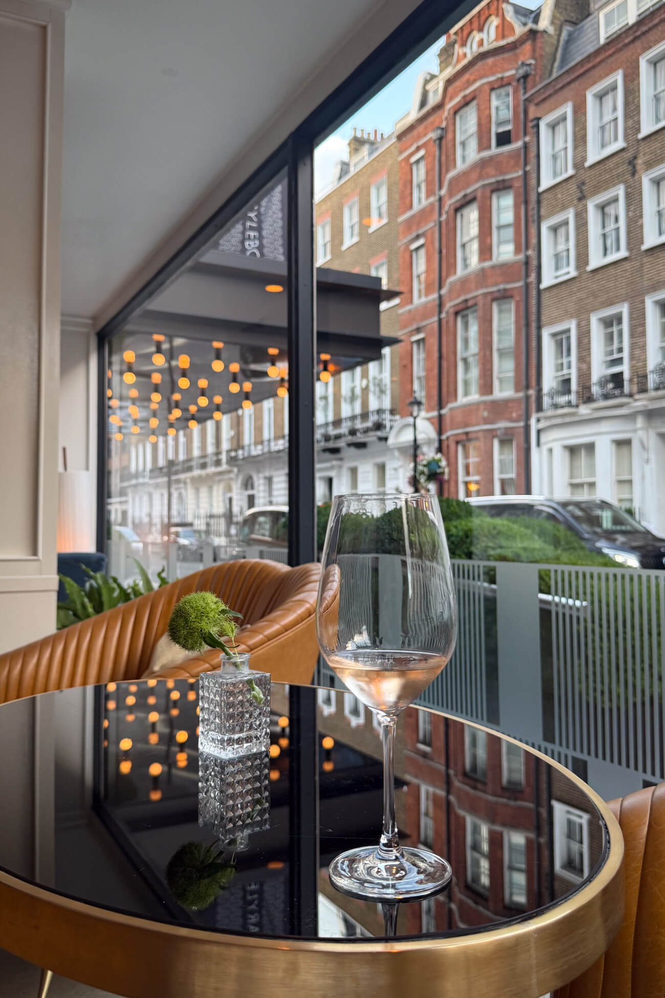 A glass of rose wine on a bar table near a window with typical Marylebone architecture in the background. This is the guest lounge/bar area of the Marylebone Hotel. 