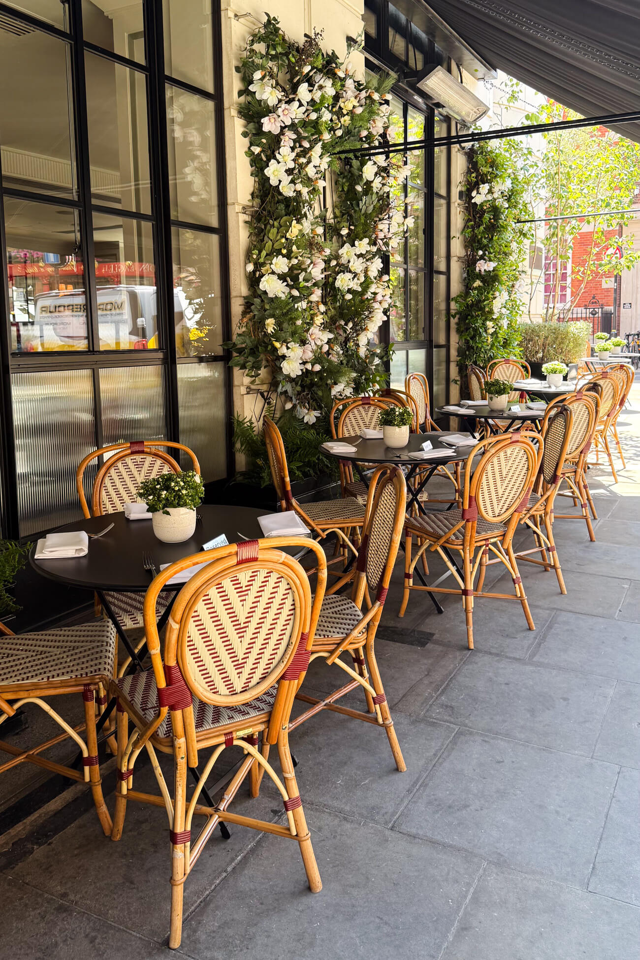 Picturesque outdoor French style bistro dining tables and chairs on a flower-lined sidewalk at the Marylebone Hotel. This is the outdoor dining area for 108 Brasserie. 