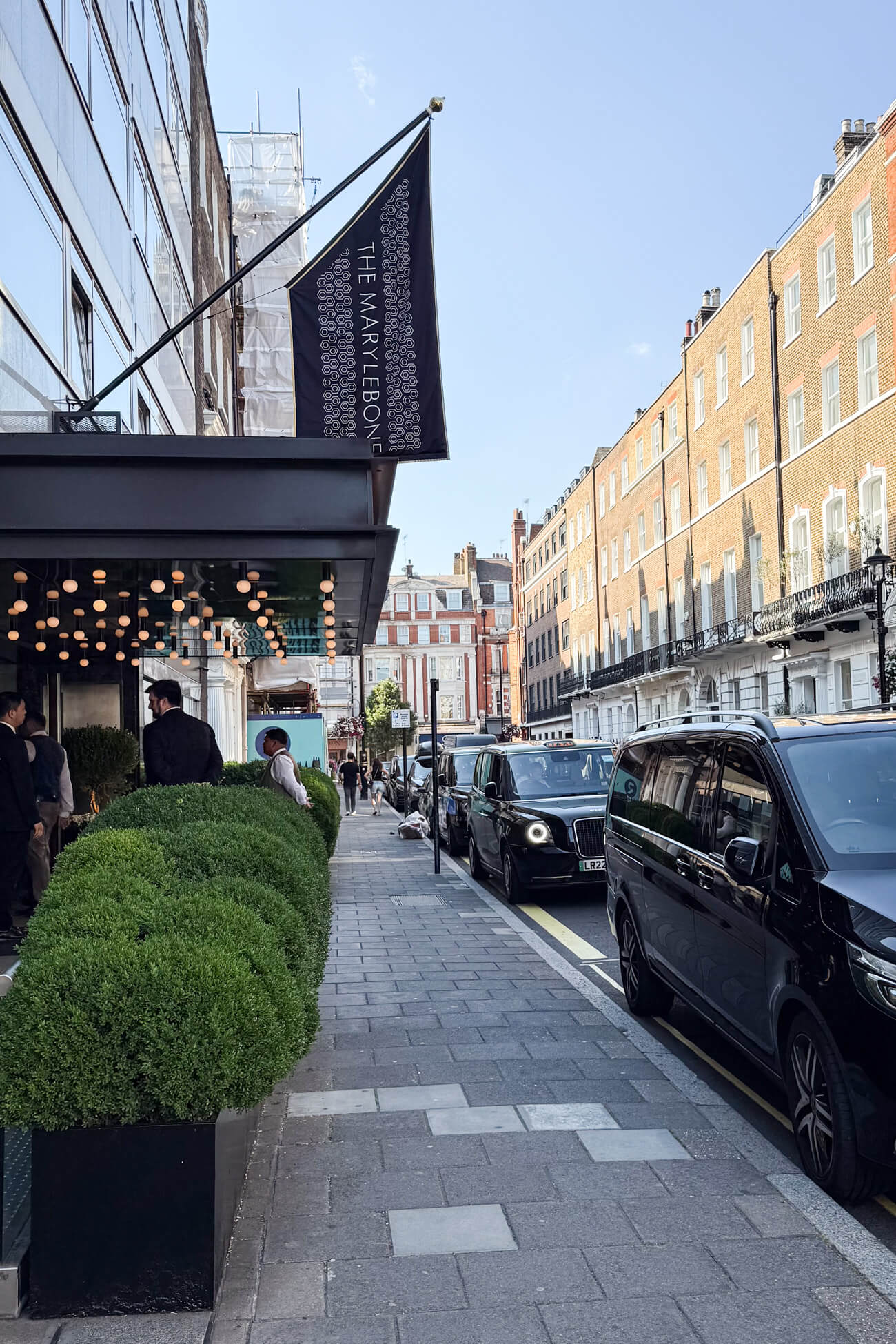 The front of The Marylebone Hotel: a black awning with lights and a black and white flag that says "The Marylebone." This is a 5-star Marylebone London boutique hotel. 
