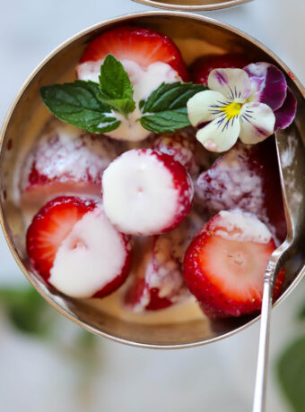 Close-up food photography of a bowl of Wimbledon strawberries and cream made at home and garnished with fresh mint and a viola.