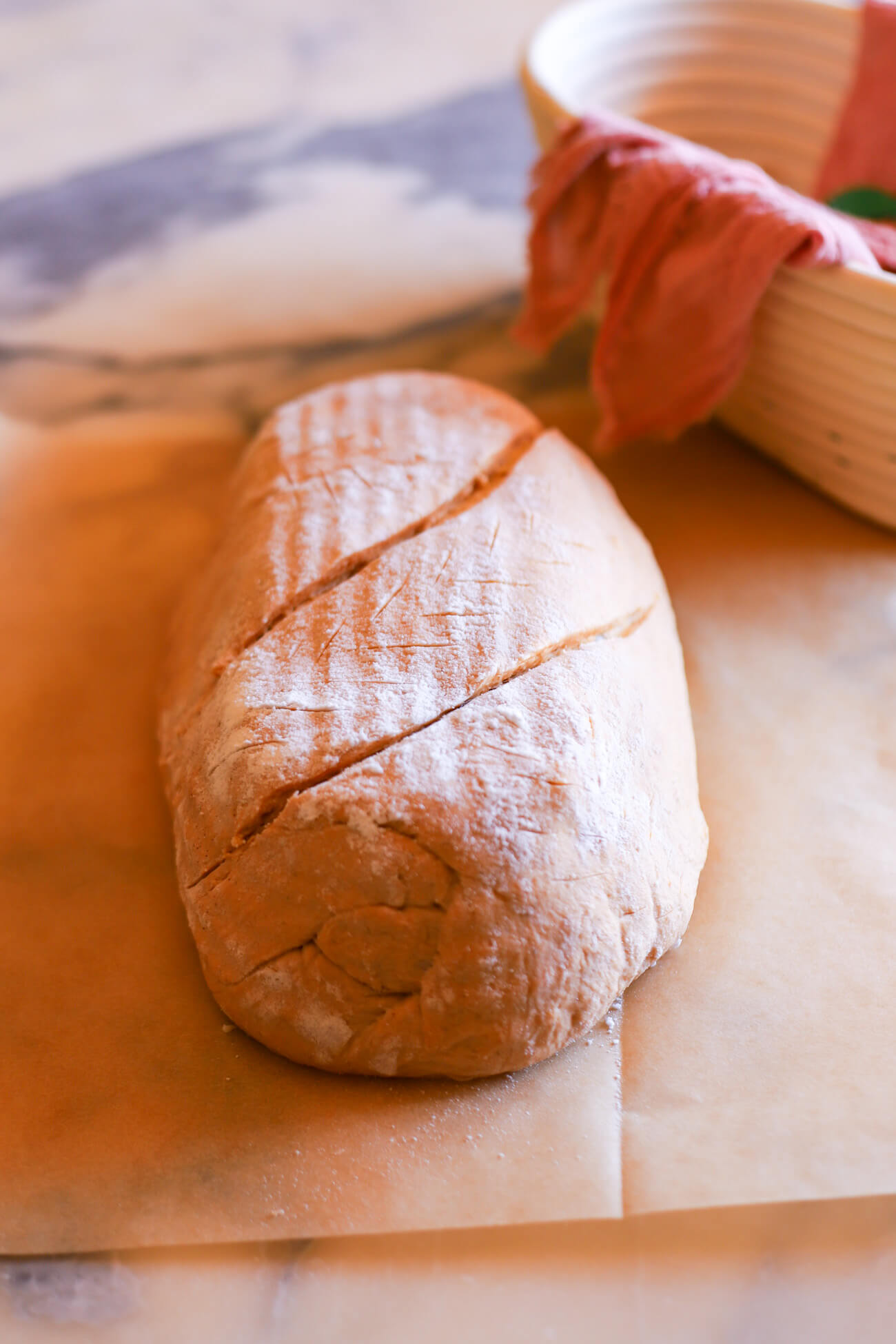 Fully proofed pumpkin sourdough bread dough on a piece of parchment paper with two diagonal slash scores.