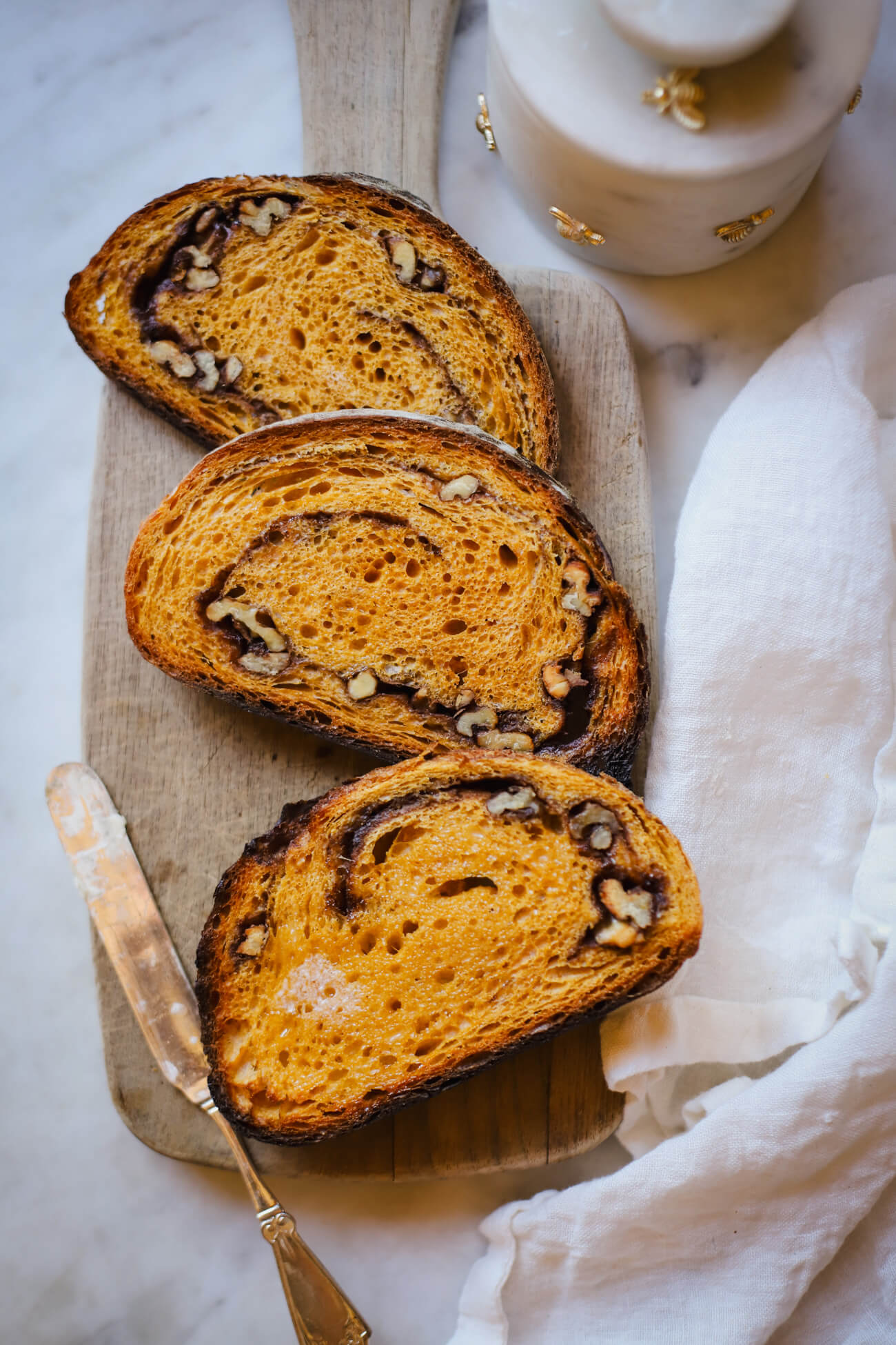 Slices of pumpkin sourdough bread with cinnamon sugar swirl and walnuts on a wooden board