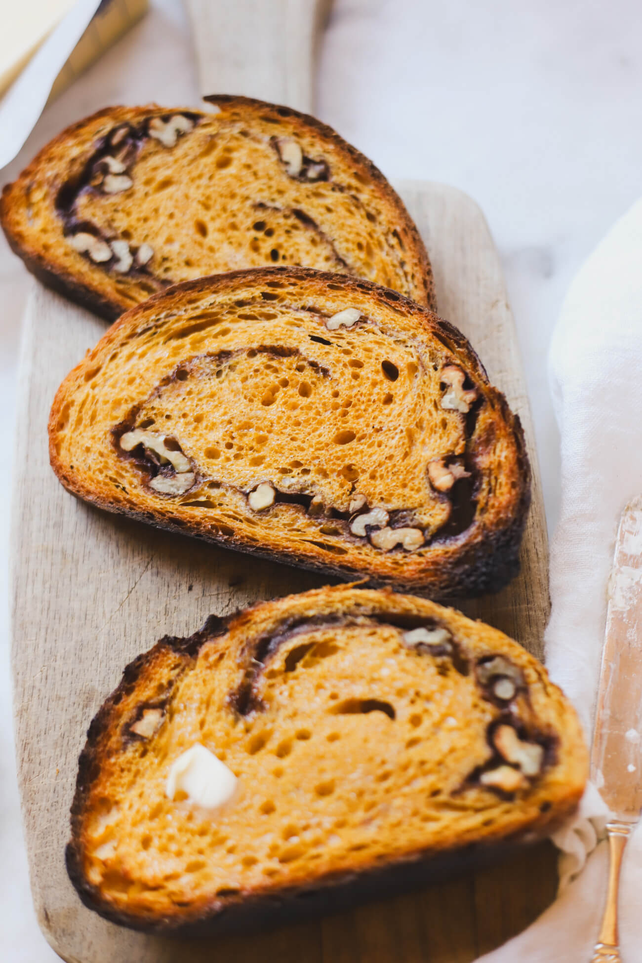 Pumpkin Sourdough Bread 3 slices of beautiful toasted pumpkin spice sourdough bread with cinnamons swirl and walnuts on a wooden cutting board.
