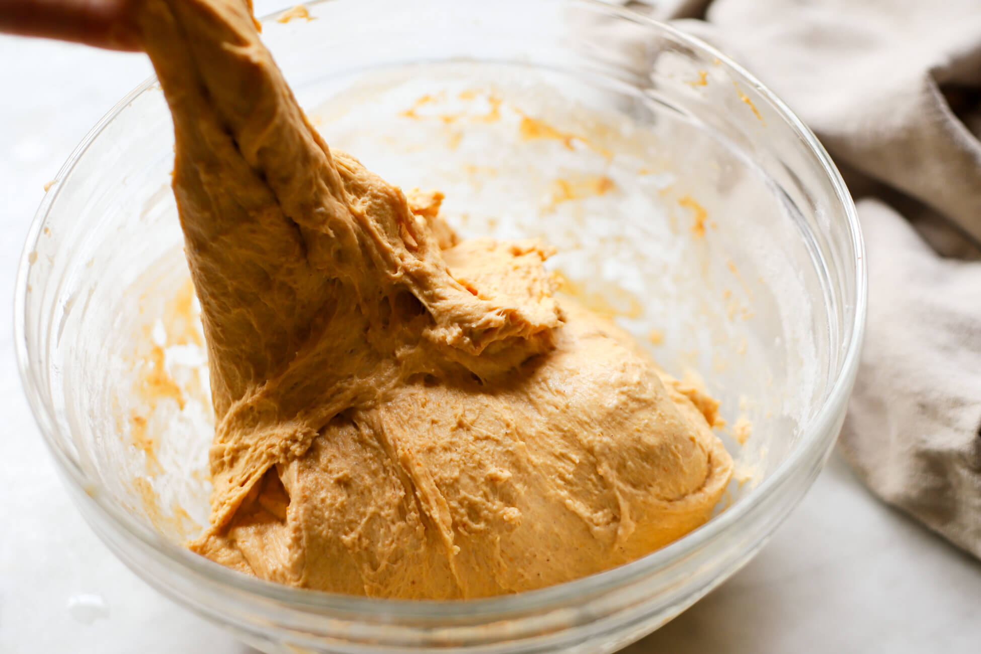 Pumpkin sourdough dough is pulled up from a glass bowl to perform "stretch and folds."