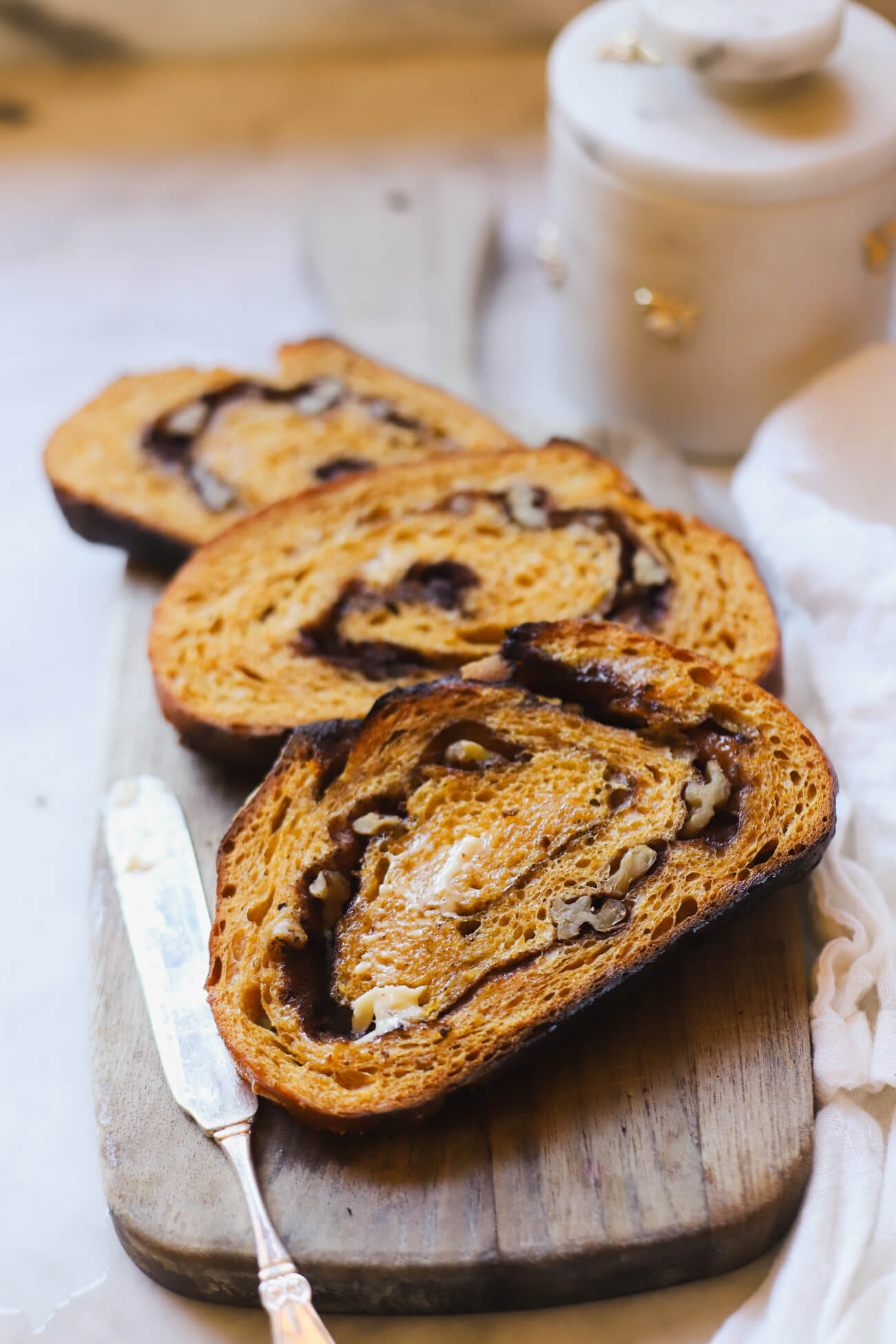 Toasted Pumpkin Sourdough Bread Toasted slices of pumpkin sourdough bread with cinnamon sugar swirl and walnuts on a wooden board with butter knife