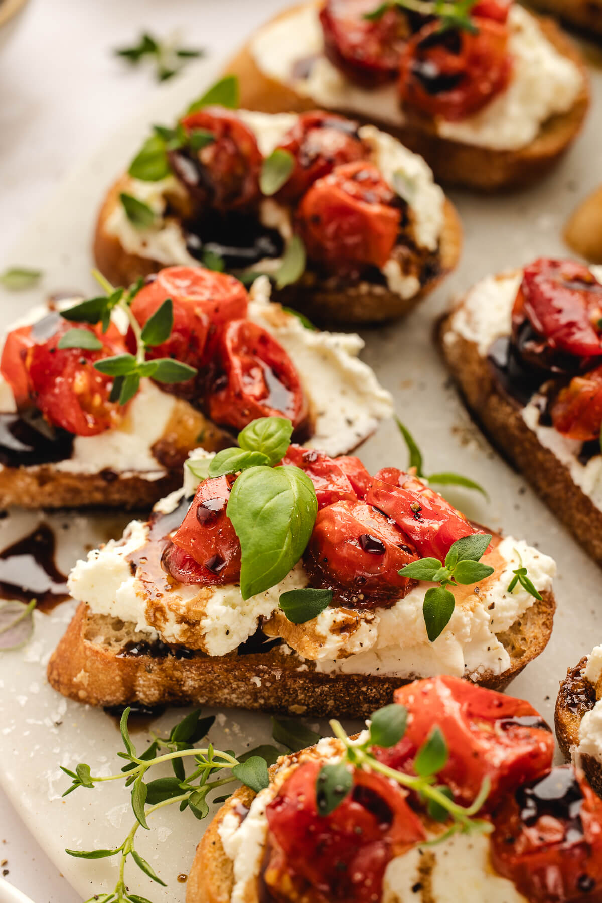Whipped Ricotta Crostini with Roasted Tomatoes Whipped ricotta crostini topped with roasted cherry tomatoes, balsamic glaze, and fresh basil on a serving platter.