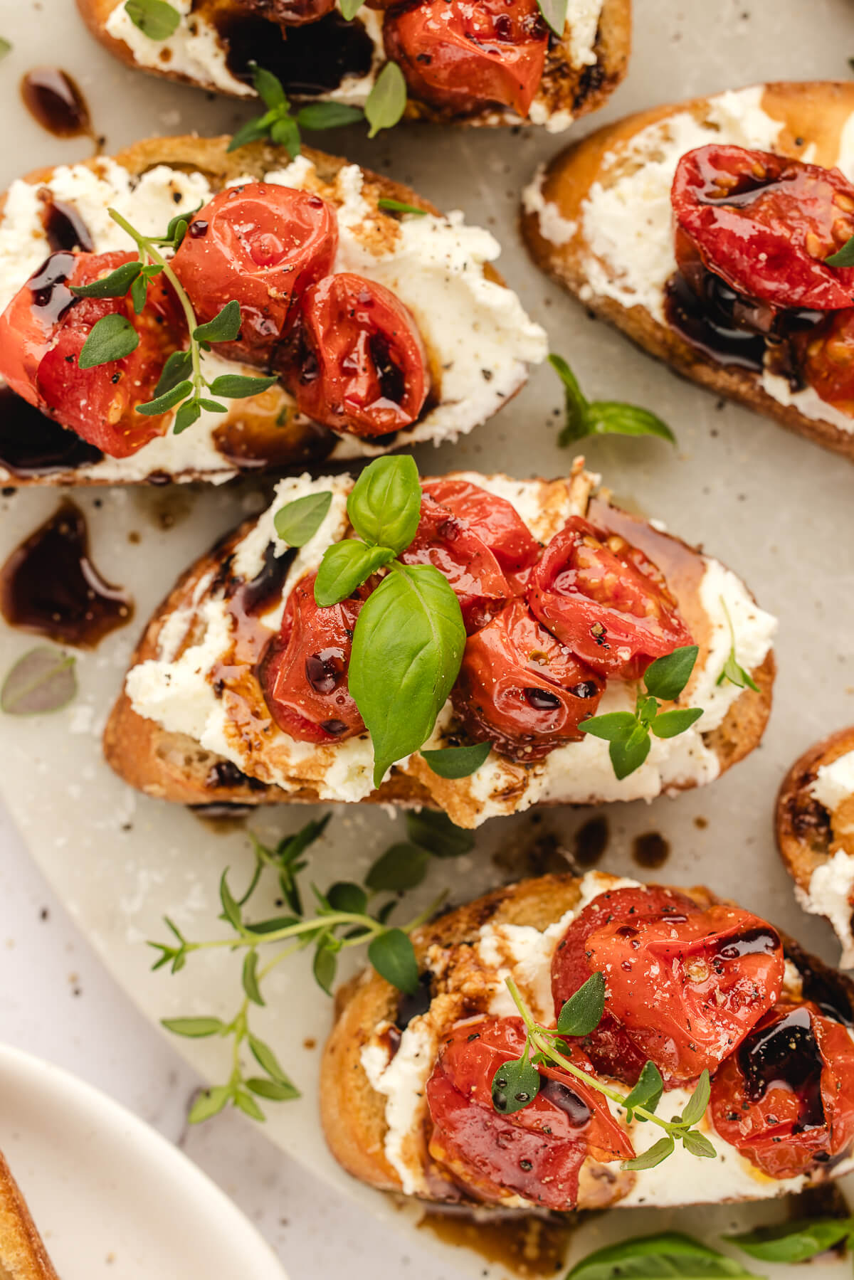 Whipped Ricotta Crostini with Roasted Tomatoes Overhead view of whipped ricotta crostini topped with roasted cherry tomatoes, balsamic glaze, and fresh basil.