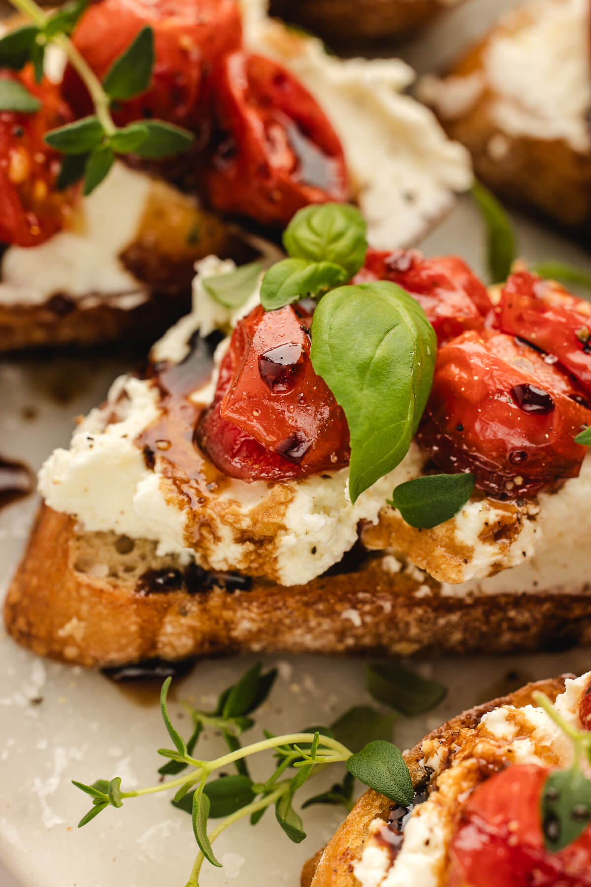 Close-up of crostini topped with whipped ricotta, roasted cherry tomatoes, balsamic and basil.