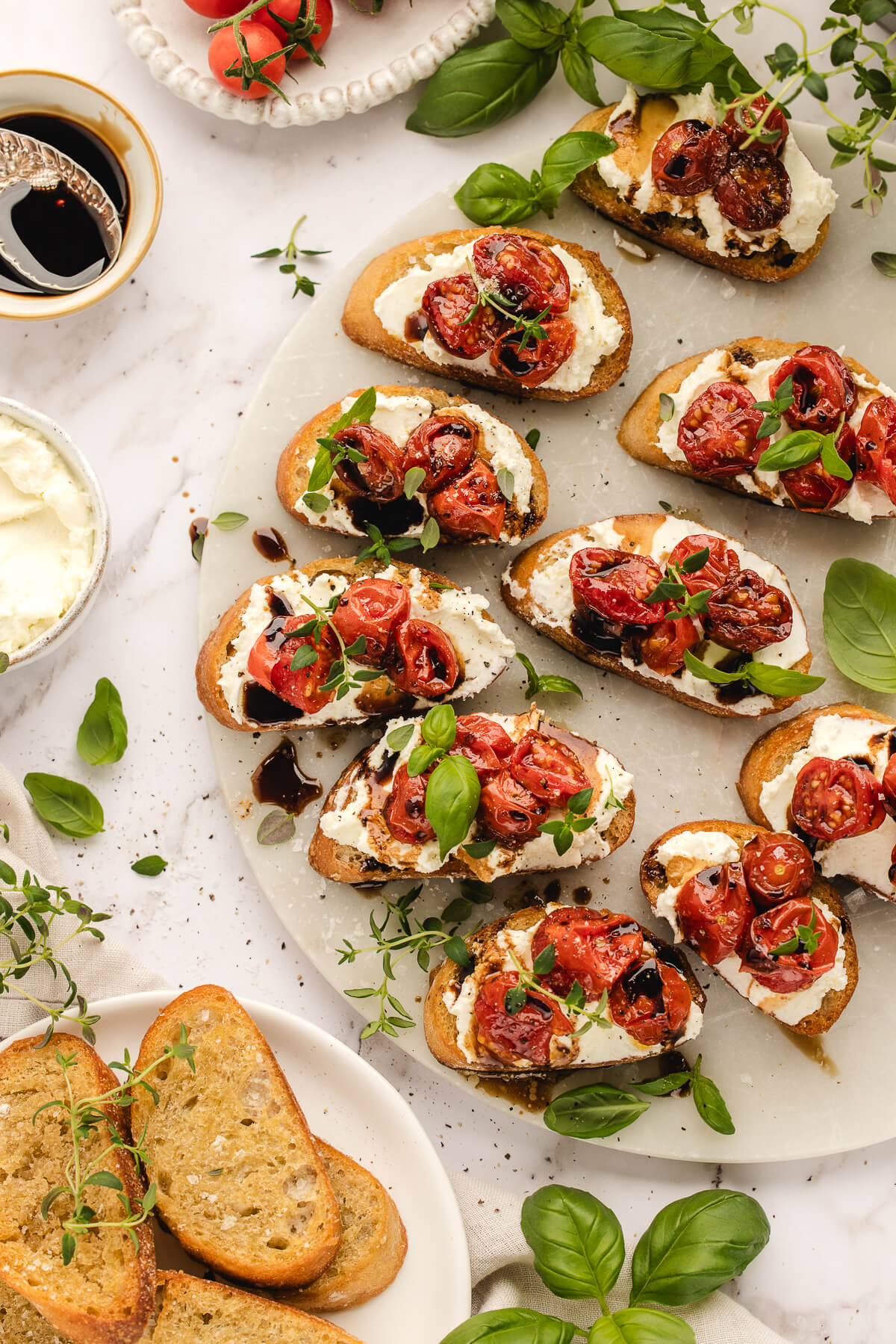 Whipped Ricotta Crostini with Roasted Cherry Tomatoes and Basil Whipped ricotta crostini with roasted cherry tomatoes and fresh basil on a marble surface with balsamic glaze and toasted baguette slices.