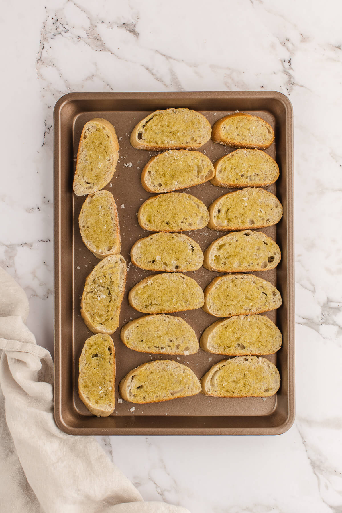 Slices of baguette on a cookie sheet with olive oil to make crostini in the oven.