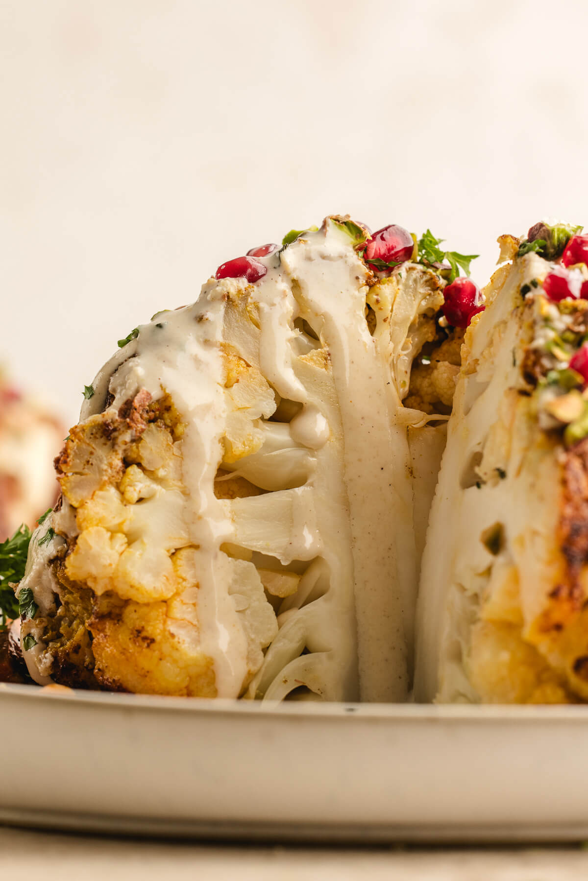 Whole roasted cauliflower sliced open to reveal its tender center, topped with creamy tahini sauce, herbs, and pomegranate seeds.