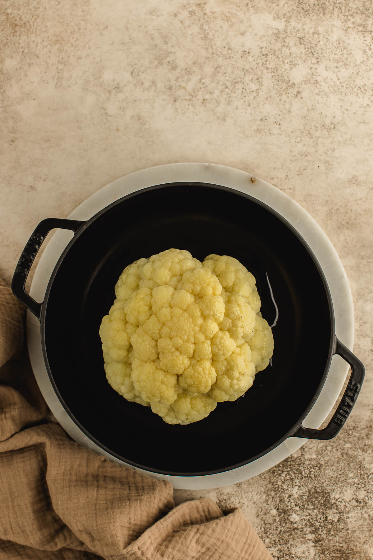 A whole cauliflower on a steamer rack in a Staub cast iron pot.