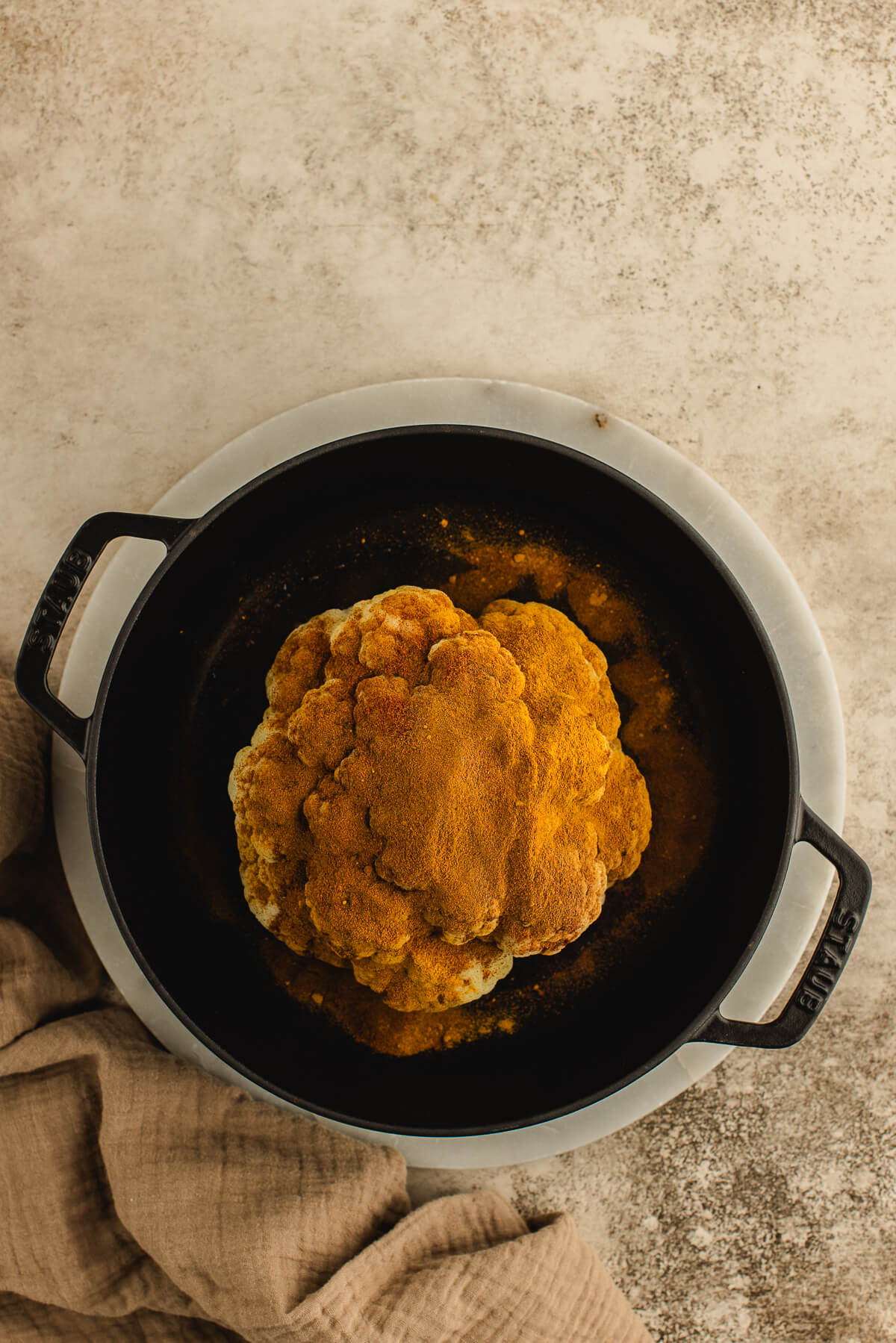 Warm spices cover a whole cauliflower in a black cast iron pot.