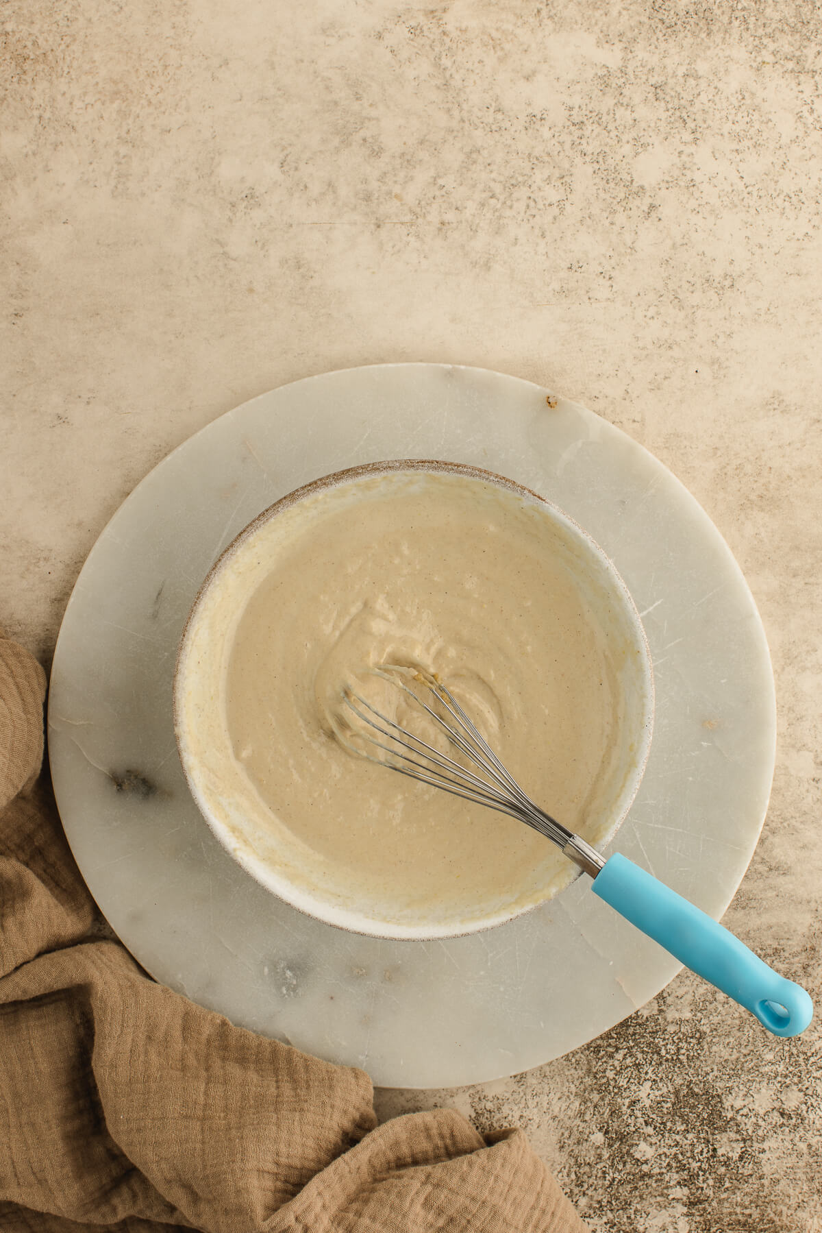 Homemade tahini sauce in a ceramic bowl with a small whisk.