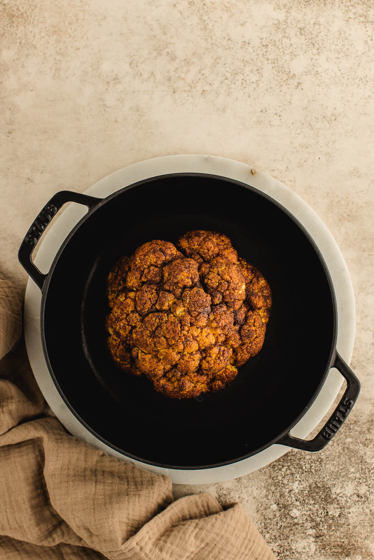 Spiced whole roasted cauliflower overhead photo in a black cast iron pot.