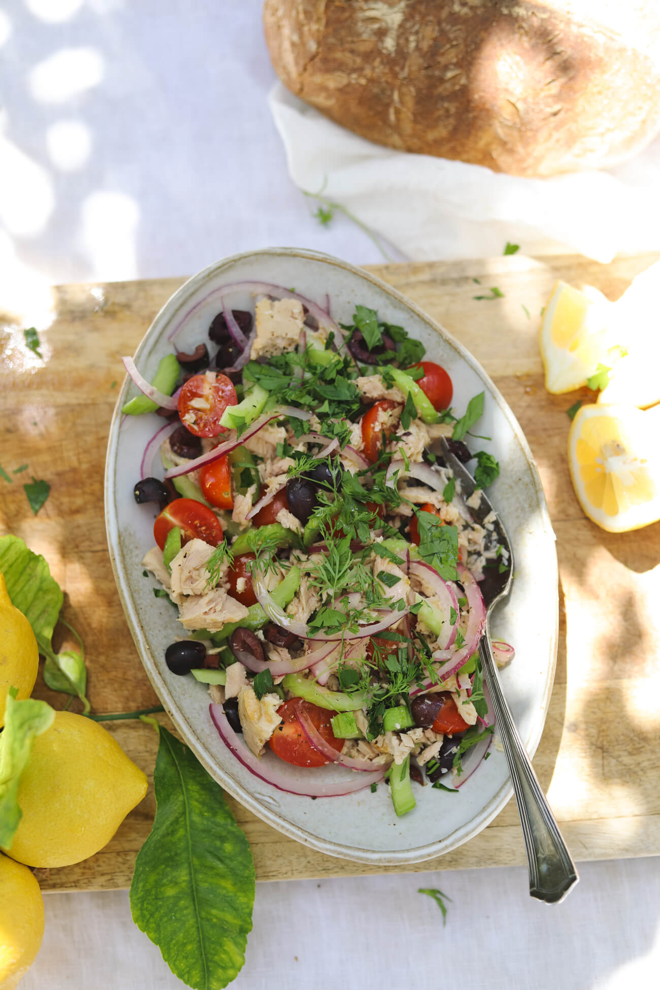 Mediterranean Tuna Salad with Lemon and Sourdough Overhead view of Mediterranean tuna salad with albacore tuna, cherry tomatoes, kalamata olives, celery, red onion, parsley, lemon wedges, and crusty sourdough bread.