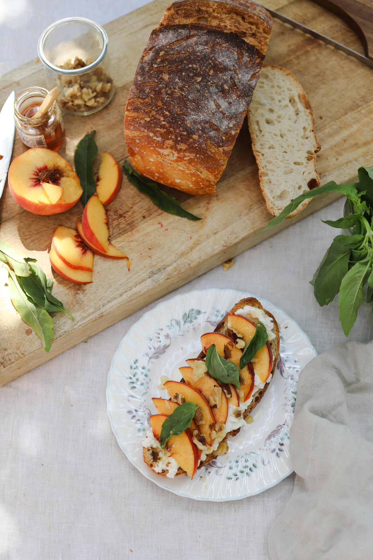 Peach Ricotta Toast with Homemade Sourdough Peach ricotta toast with homemade sourdough, fresh peaches, whipped honey ricotta, basil, and walnuts alongside the ingredients on a wooden board.