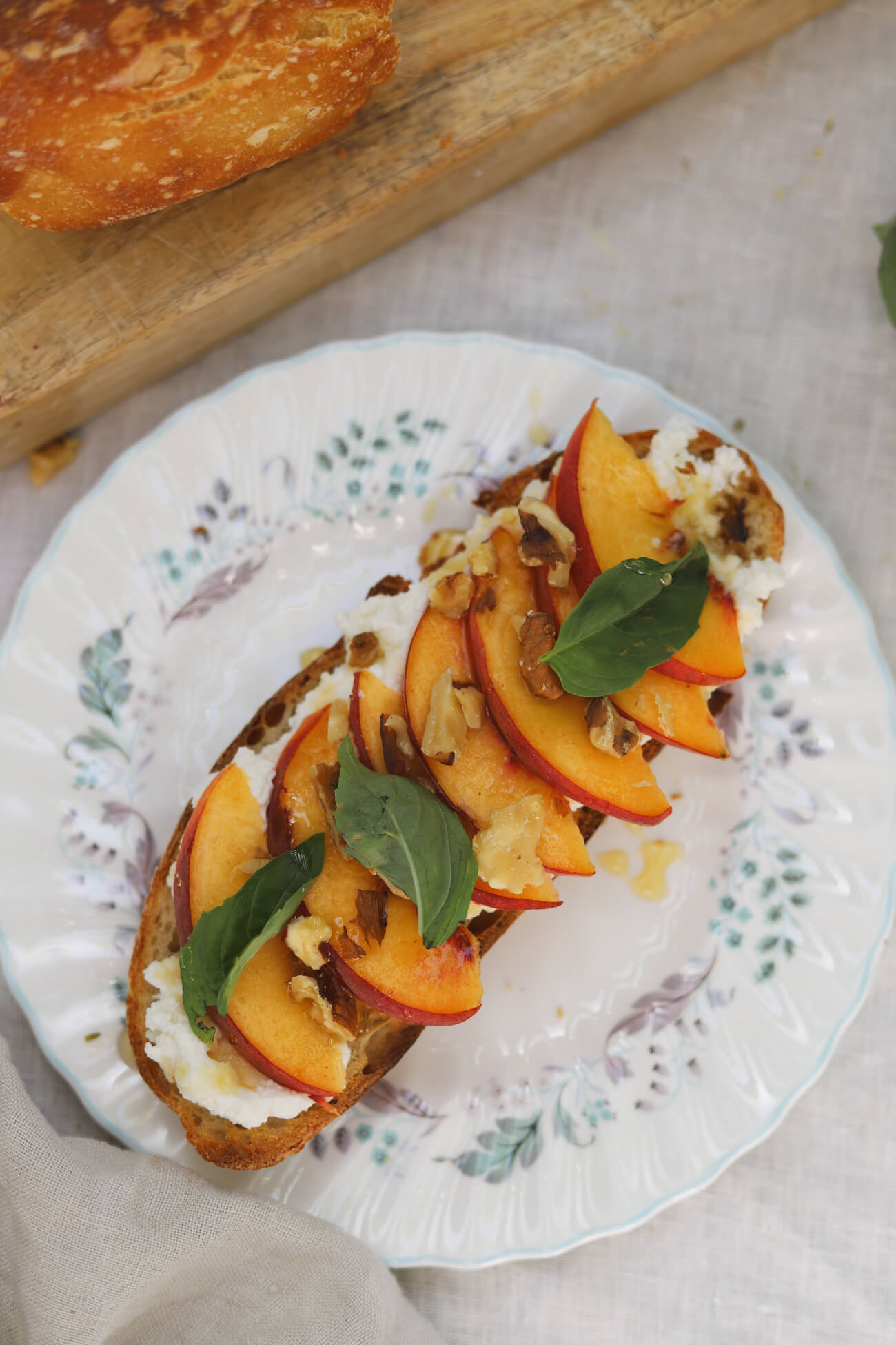 Peach Ricotta Toast with Homemade Sourdough Overhead view of peach ricotta toast on homemade sourdough topped with whipped honey ricotta, fresh peaches, basil, walnuts, and honey.