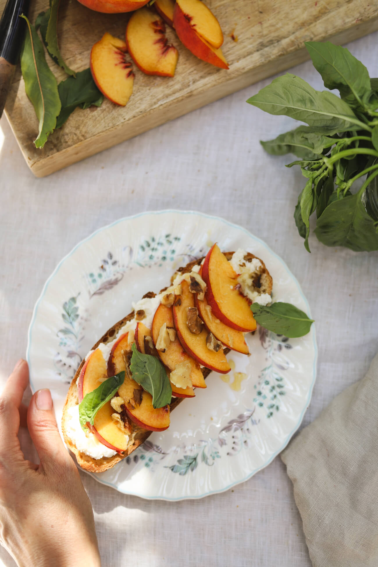 Peach Ricotta Toast with Whipped Honey Ricotta Peach ricotta toast made with homemade sourdough, whipped honey ricotta, fresh peaches, basil, toasted walnuts, and honey on a white plate.