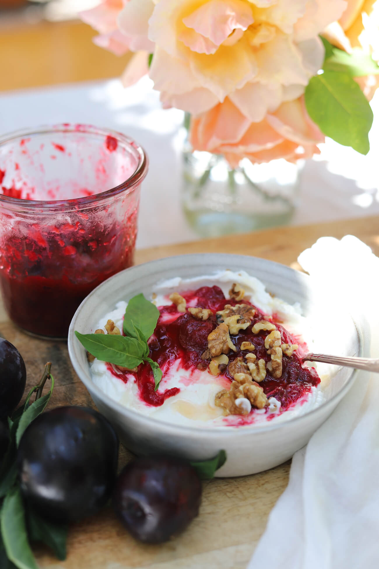 Homemade Roasted Plum Compote with Greek Yogurt Greek yogurt topped with homemade roasted plum compote, walnuts, and fresh basil with a jar of plum compote in the background