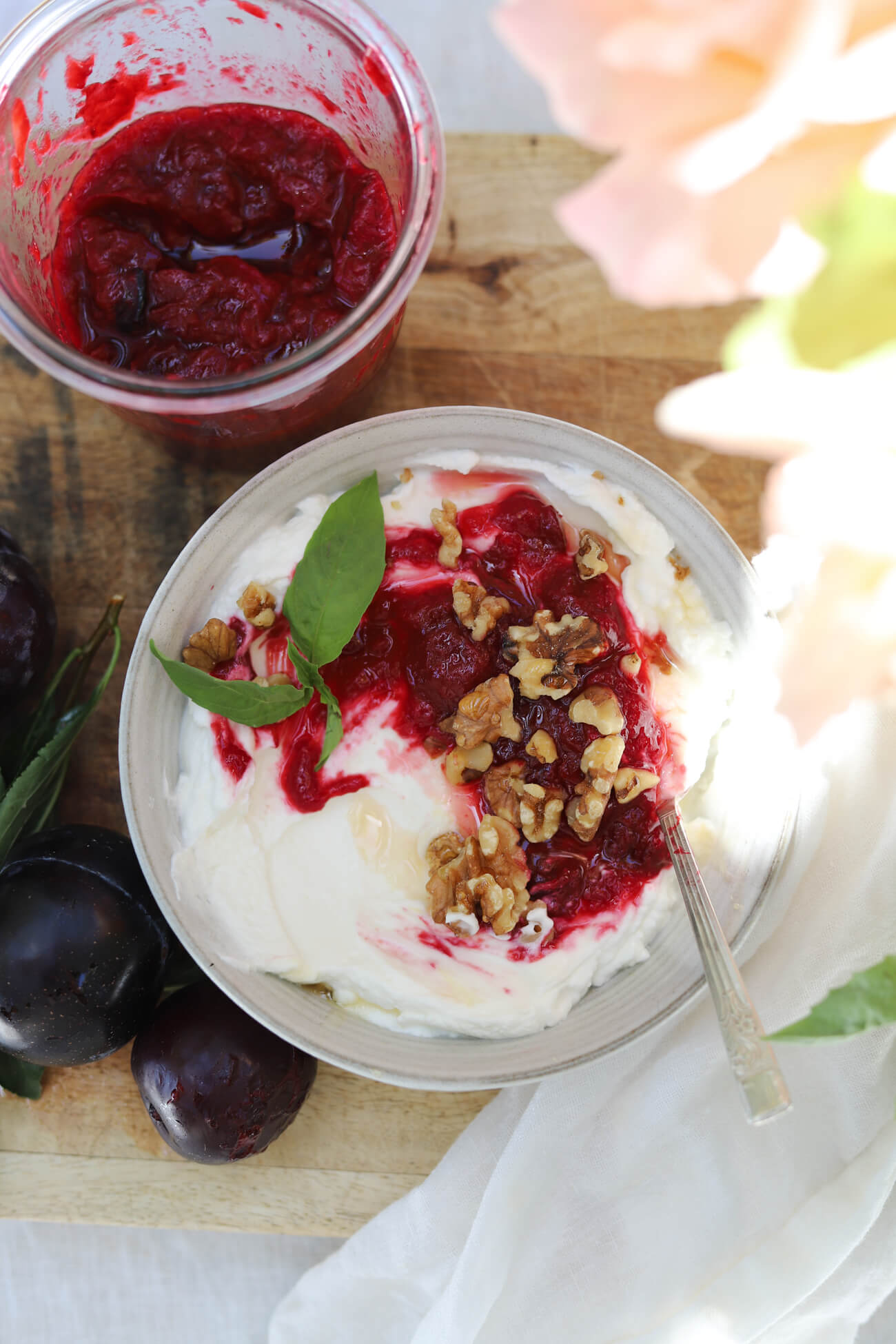 Roasted Plum Compote with Greek Yogurt Greek yogurt topped with homemade roasted plum compote, walnuts, and fresh basil, served with a jar of plum compote.