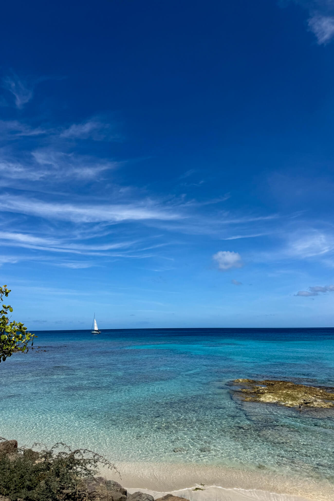 Mustique Island Beach Crystal-clear turquoise Caribbean water off the coast of Mustique Island, with a sailboat on the horizon beneath a blue sky.