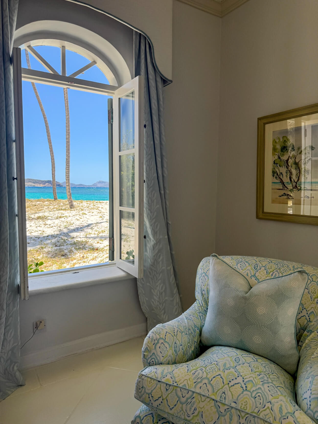 Mustique Island West Indies Villa View from a beachfront villa on Mustique Island through an open arched window, overlooking palm trees, white sand, and the turquoise Caribbean Sea.