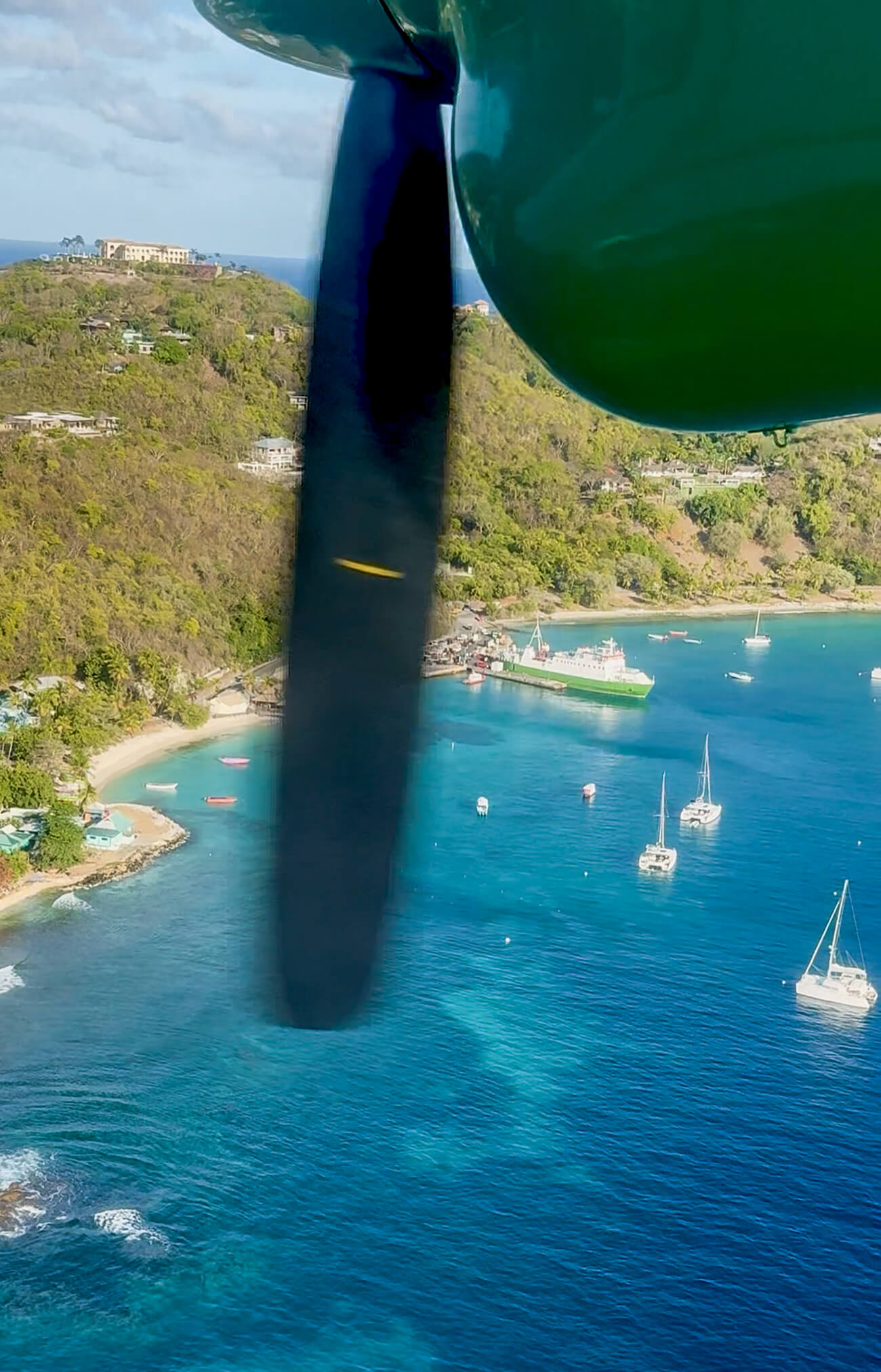 Flying into Mustique Island Aerial view of Mustique Island from a small plane, with turquoise Caribbean water, sailboats, green hills, and the coastline below.